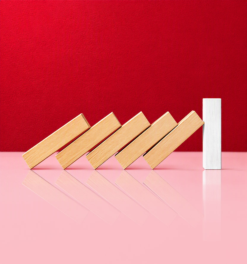 Wooden domino-like blocks are falling in sequence toward a single upright white block that stops the chain reaction.