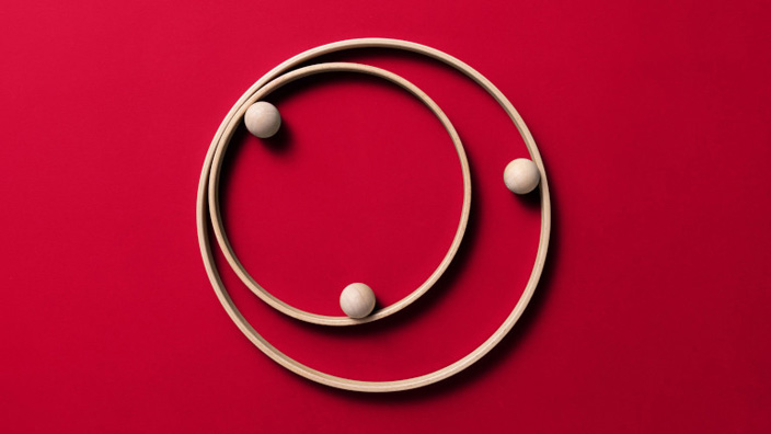 Three light-colored spheres positioned along two concentric circular tracks against a red background.